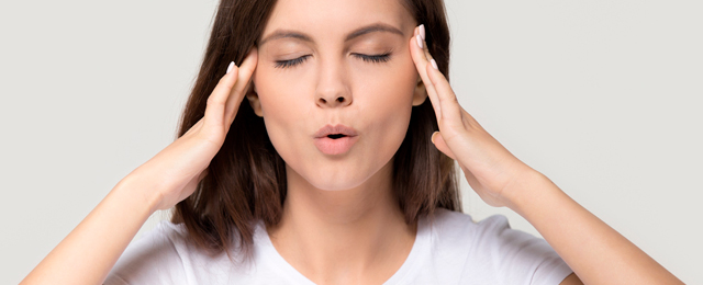 Mulher com os olhos fechados e as mãos nas têmporas, a respirar fundo, representando técnicas para lidar com ataques de pânico.