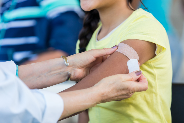 Profissional de saúde a aplicar um penso no braço de uma criança após vacinação, promovendo cuidados preventivos de saúde.