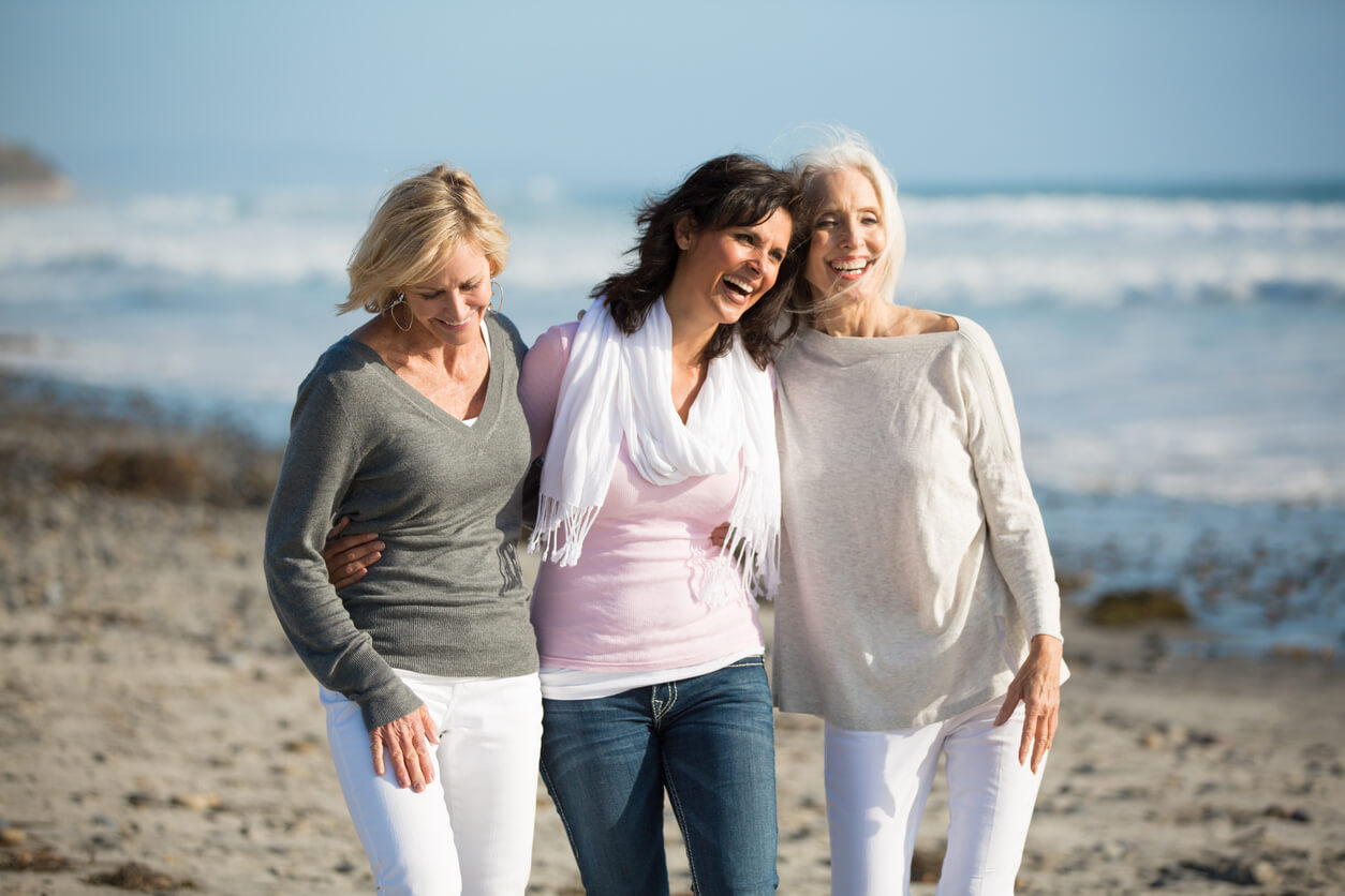 Três mulheres a passear à beira-mar, a viver de forma saudável esta nova fase de vida que é a menopausa.