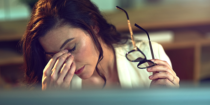 Mulher com ar cansado, a esfregar os olhos, enquanto segura nos óculos. Sinal da alteração de humor desta nova fase de vida que é a menopausa.